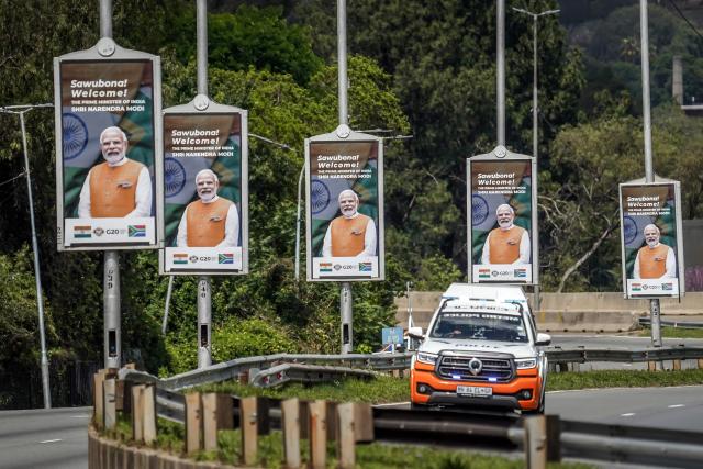 A vehicle of the Johannesburg Metro Police Department (JMPD) drives past banners bearing the photograph of India's Prime Minister Narendra Modi on a major freeway heading toward the Nasrec Expo Centre in Johannesburg on November 22, 2025, ahead of the opening of the G20 Leader's Summit. (Photo by Zinyange Auntony / AFP)