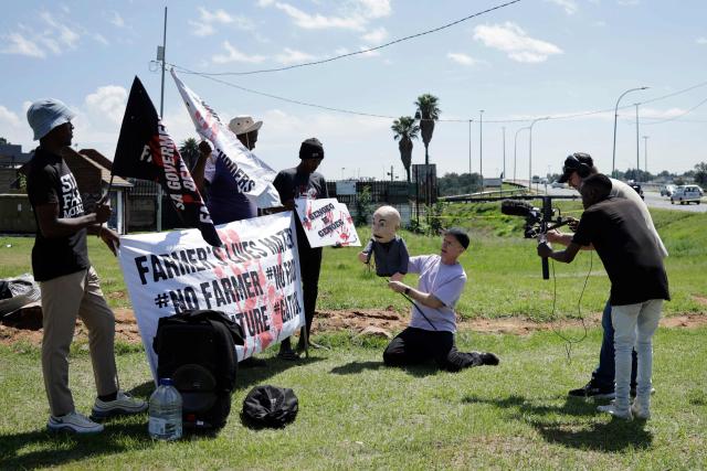 South African Comedian Conrad Koch gestures with his puppet Chester Missing (3rd R) as they talk to Farmer Lives Matter protesters next to a road near the Nasrec Expo Centre in Johannesburg on November 22, 2025 ahead of the opening of the G20 Leaders' Summit. (Photo by EMMANUEL CROSET / AFP)
