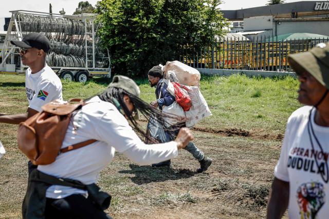 TOPSHOT - A recycler (C) walks past members of the vigilante group known as Operation Dudula, which means "push back" in Zulu, during a protest near the Nasrec Expo Centre in Johannesburg on November 22, 2025, ahead of the opening of the G20 Leaders’ Summit. Operation Dudula is protesting against the South African government turning a blind eye to corruption, joblessness, rising crime, illegal immigration and failing public services. (Photo by Marco Longari / AFP)