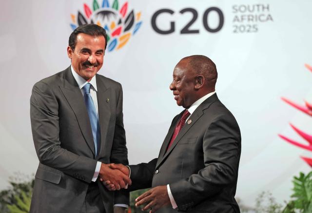 South African President Cyril Ramaphosa (R) welcomes Qatar's Emir Sheikh Tamim bin Hamad Al Thani as he arrives for the opening of the G20 Leaders' Summit at the Nasrec Expo Centre in Johannesburg on November 22, 2025. (Photo by Halden KROG / POOL / AFP)