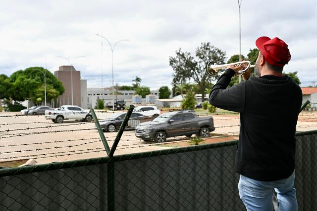 Trumpeter Fabiano Leitao, a supporter of Brazilian President Luiz Inacio Lula da Silva known as Fabiano Trompetista, plays the funeral march in front of the Brazilian Federal Police Headquarters in Brasilia on November 22, 2025, where former President Jair Bolsonaro was transferred earlier. Ex-President Bolsonaro was taken from house arrest into police custody early November 22, as he is considered a flight risk, according to a Supreme Court ruling. Judge Alexandre de Moraes said Bolsonaro, who in September had been sentenced to 27 years in prison over a botched coup bid but has yet to begin serving his term, was a "high flight risk". (Photo by Evaristo SA / AFP)