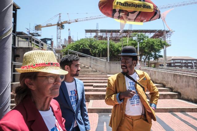 Artivist Crosby Luhlungwane wears a colorful suit to mimic opulence as he holds a balloon and gathers with others during a Greenpeace protest calling for a tax on the super-rich at Constitution Hill in Johannesburg on November 22, 2025, during the G20 Leaders' Summit. (Photo by Zinyange Auntony / AFP)