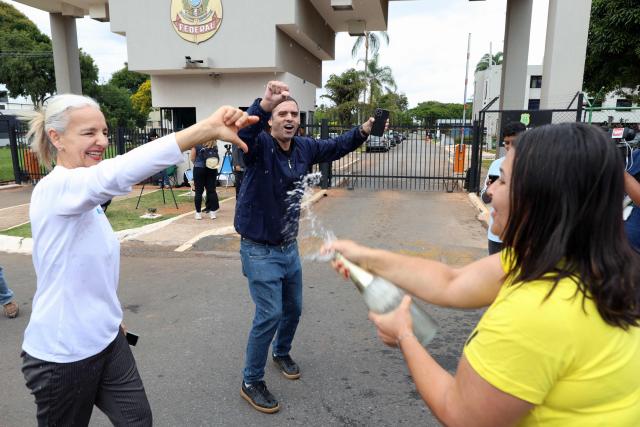 Protesters celebrate the arrest of former Brazilian President Jair Bolsonaro with drinks in front of Bolsonaro's supporters outside the Brazilian Federal Police headquarters in Brasilia on November 22, 2025, where the ex-president had been transferred earlier. Ex-President Jair Bolsonaro was taken from house arrest into police custody early on November 22, as he is considered a flight risk according to a Supreme Court ruling. Judge Alexandre de Moraes said Bolsonaro, who in September had been sentenced to 27 years in prison over a botched coup bid but has yet to begin serving his term, was a "high flight risk". (Photo by Sergio Lima / AFP)