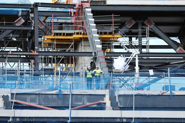 Two workers watch the game from the under-construction stands during the Spanish league football match between FC Barcelona and Athletic Club Bilbao at Camp Nou Stadium in Barcelona on November 22, 2025. (Photo by Josep LAGO / AFP)