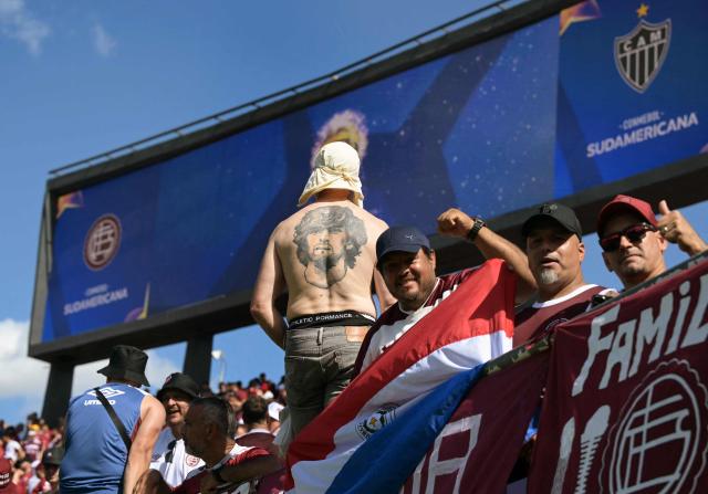 A fan of Lanus bearing a tattoo depicting the late football legend Diego Armando Maradona waits for the start of the Copa Sudamericana final football match between Argentina's Lanus and Brazil's Atletico Mineiro at the Defensores del Chaco stadium in Asuncion on November 22, 2025. (Photo by JUAN MABROMATA / AFP)