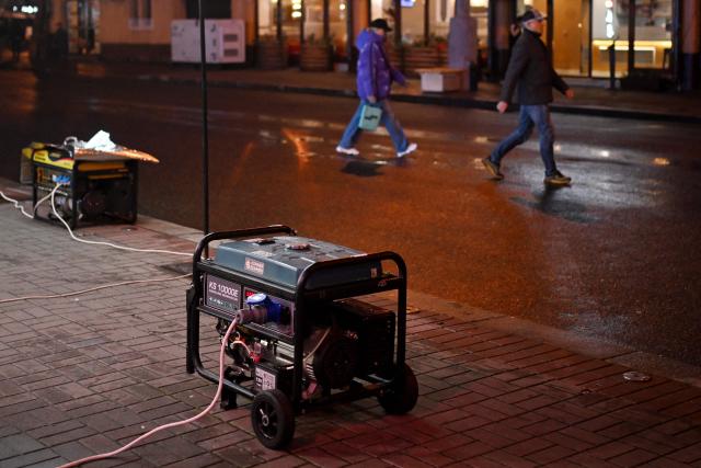 Pedestrians walk past power generators supplying electricity to restaurants during blackout hours in Kyiv on November 22, 2025, amid the Russian invasion of Ukraine. (Photo by Sergei GAPON / AFP)