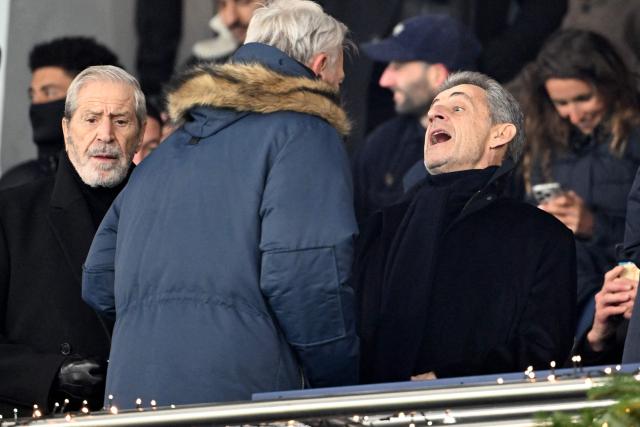 France's former president Nicolas Sarkozy (R), who was allowed to go free after serving three weeks in jail despite being handed a five-year prison sentence after his conviction for allowing aides to seek to collect money for his 2007 presidential election campaign from Libyan leader Moamer Kadhafi, speaks with an attendee next to French businessman Jean-Claude Darmon (L) in the stand prior to the kick off of the French L1 football match between Paris Saint-Germain (PSG) and Le Havre AC at the Parc des Princes stadium in Paris, on November 22, 2025. (Photo by Bertrand GUAY / AFP)