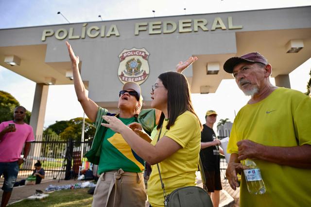 Supporters of former Brazilian President Jair Bolsonaro pray outside the Brazilian Federal Police headquarters in Brasilia on November 22, 2025, where the ex-president had been transferred earlier. Ex-President Jair Bolsonaro was taken from house arrest into police custody early on November 22, as he is considered a flight risk according to a Supreme Court ruling. Judge Alexandre de Moraes said Bolsonaro, who in September had been sentenced to 27 years in prison over a botched coup bid but has yet to begin serving his term, was a "high flight risk". (Photo by Evaristo Sa / AFP)