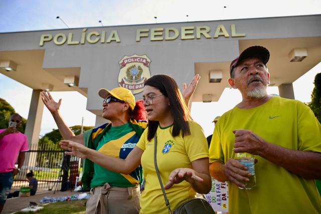 Supporters of former Brazilian President Jair Bolsonaro pray outside the Brazilian Federal Police headquarters in Brasilia on November 22, 2025, where the ex-president had been transferred earlier. Ex-President Jair Bolsonaro was taken from house arrest into police custody early on November 22, as he is considered a flight risk according to a Supreme Court ruling. Judge Alexandre de Moraes said Bolsonaro, who in September had been sentenced to 27 years in prison over a botched coup bid but has yet to begin serving his term, was a "high flight risk". (Photo by Evaristo Sa / AFP)