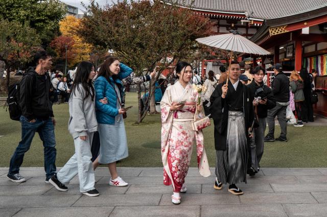 Asian tourists pose during a visit to Sensoji Temple in the Asakusa district of central Tokyo on November 23, 2025. (Photo by Philip FONG / AFP)