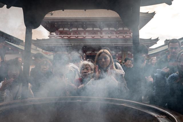 Asian tourists baths in incense smoke during a visit to Sensoji Temple in the Asakusa district of central Tokyo on November 23, 2025. (Photo by Philip FONG / AFP)