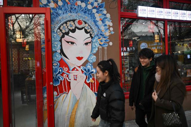 People walk past a mural outside a restaurant in Beijing on November 23, 2025. (Photo by Pedro PARDO / AFP)