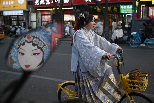 A woman wears a traditional Chinese costume as she rides a bicycle along the street in Beijing on November 23, 2025. (Photo by Pedro PARDO / AFP)