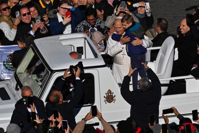Pope Leo XIV (C) embraces a child as he stands on the popemobile while leaving at the end of the Jubilee of Choirs and Choral Society mass at St Peter's Square, in The Vatican, on November 23, 2025. (Photo by Andreas SOLARO / AFP)