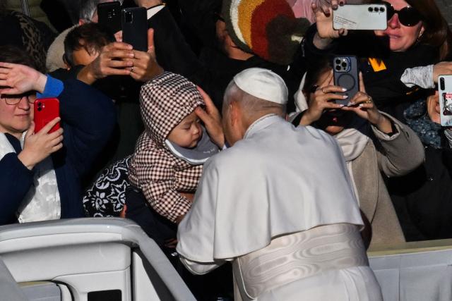 Pope Leo XIV (C) blesses a baby as he stands on the popemobile while leaving at the end of the Jubilee of Choirs and Choral Society mass at St Peter's Square, in The Vatican, on November 23, 2025. (Photo by Andreas SOLARO / AFP)