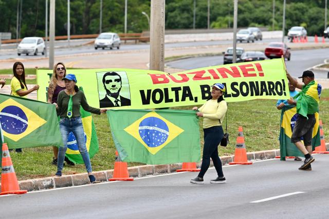 Supporters of former Brazil's President (2019–2023) Jair Bolsonaro hold Brazilian flags during a demonstration in front of the Federal Police headquarters, where Bolsonaro is being held, in Brasнlia, on November 23, 2025. Ex-President Jair Bolsonaro -who in September had been sentenced to 27 years in prison over a botched coup bid but has yet to begin serving his term- was taken from house arrest into police custody on November 22 as he is considered a flight risk according to a Supreme Court ruling. (Photo by Evaristo Sa / AFP)