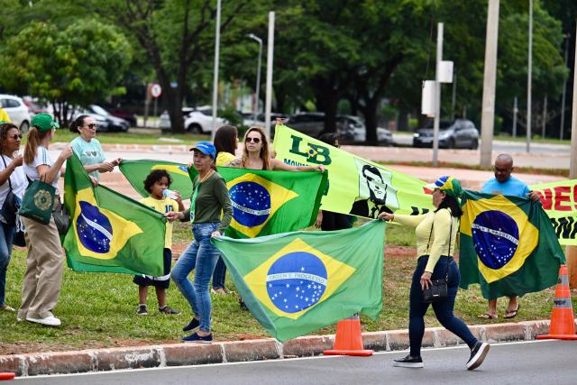 Supporters of former Brazil's President (2019–2023) Jair Bolsonaro hold Brazilian flags during a demonstration in front of the Federal Police headquarters, where Bolsonaro is being held, in Brasнlia, on November 23, 2025. Ex-President Jair Bolsonaro -who in September had been sentenced to 27 years in prison over a botched coup bid but has yet to begin serving his term- was taken from house arrest into police custody on November 22 as he is considered a flight risk according to a Supreme Court ruling. (Photo by Evaristo Sa / AFP)