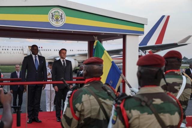 Gabon's President Brice Oligui Nguema (L) and France’s President Emmanuel Macron (2nd L) inspect the guard of honour upon Macron's arrival at the Leon-Mba International Airport in Libreville on November 23, 2025. (Photo by Ludovic MARIN / AFP)