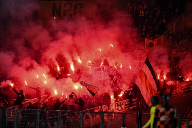 Lorient's supporters wave flags and burn flares during the French L1 football match between FC Nantes and FC Lorient at the Stade de la Beaujoire–Louis-Fonteneau in Nantes, western France, on November 23, 2025. (Photo by Sebastien Salom-Gomis / AFP)