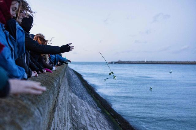 Mourners  throw roses into the sea as they take part in a commemorative march to pay tribute to the 27 victims of a migrant boat shipwreck in the English Channel which occured on November 24, 2021, in Calais, northern France, on November 23, 2025. (Photo by Sameer Al-DOUMY / AFP)
