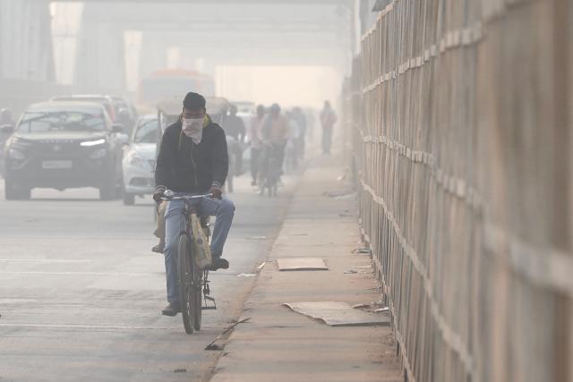 A man with his face covered with a cloth rides a bicycle on a bridge amid smoggy conditions in Varanasi on November 24, 2025. (Photo by Niharika KULKARNI / AFP)