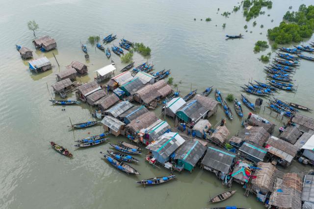 In this aerial photograph taken on July 12, 2025, fishing boats lie moored beside stilt houses along the shores of Shibsa river at Jhulonto Para, a village vulnerable to rising sea levels in Khulna district. On Bangladesh's coast, where mighty Himalayan rivers meet the sea, water defines every rhythm of life and every struggle. For the millions living in the ecologically sensitive deltas of mudflats and mangrove forests, finding clean drinking water has become an escalating challenge. Rising seas driven by climate change are swallowing low-lying areas, while stronger storms push saltwater further inland, turning wells and lakes brackish, according to government scientists. (Photo by Muhammad Amdad HOSSAIN / AFP) / To go with 'BANGLADESH-ENVIRONMENT-CLIMATE-WATER, REPORTAGE' by Muhammad Amdad HOSSAIN