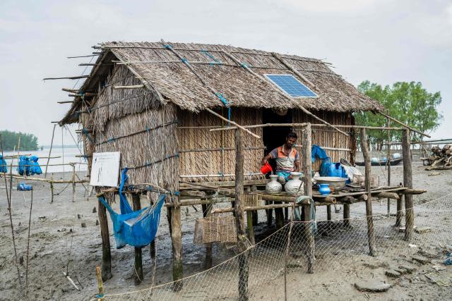 In this photograph taken on July 13, 2025, a climate-displaced man pours collected rainwater into pots at his stilt house in Jhulonto Para, a village vulnerable to rising sea levels in Khulna district. On Bangladesh's coast, where mighty Himalayan rivers meet the sea, water defines every rhythm of life and every struggle. For the millions living in the ecologically sensitive deltas of mudflats and mangrove forests, finding clean drinking water has become an escalating challenge. Rising seas driven by climate change are swallowing low-lying areas, while stronger storms push saltwater further inland, turning wells and lakes brackish, according to government scientists. (Photo by Muhammad Amdad HOSSAIN / AFP) / To go with 'BANGLADESH-ENVIRONMENT-CLIMATE-WATER, REPORTAGE' by Muhammad Amdad HOSSAIN