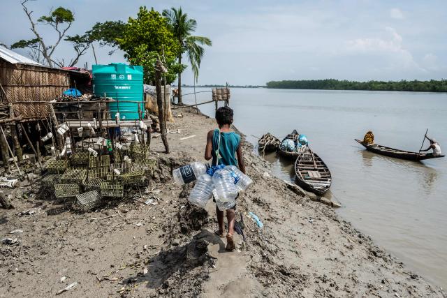 In this photograph taken on July 13, 2025, Torikul, a climate-displaced child carries plastic bottles to fetch drinking water from a distant market at Jhulonto Para, a village vulnerable to rising sea levels in Khulna district. On Bangladesh's coast, where mighty Himalayan rivers meet the sea, water defines every rhythm of life and every struggle. For the millions living in the ecologically sensitive deltas of mudflats and mangrove forests, finding clean drinking water has become an escalating challenge. Rising seas driven by climate change are swallowing low-lying areas, while stronger storms push saltwater further inland, turning wells and lakes brackish, according to government scientists. (Photo by Muhammad Amdad HOSSAIN / AFP) / To go with 'BANGLADESH-ENVIRONMENT-CLIMATE-WATER, REPORTAGE' by Muhammad Amdad HOSSAIN