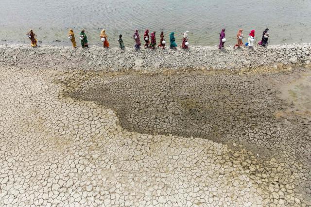 In this photograph taken on April 25, 2025, women carrying pots walk along the parched shores of Kholpetua river to fetch drinking water at Parshemari village in Khulna district. On Bangladesh's coast, where mighty Himalayan rivers meet the sea, water defines every rhythm of life and every struggle. For the millions living in the ecologically sensitive deltas of mudflats and mangrove forests, finding clean drinking water has become an escalating challenge. Rising seas driven by climate change are swallowing low-lying areas, while stronger storms push saltwater further inland, turning wells and lakes brackish, according to government scientists. (Photo by Muhammad Amdad HOSSAIN / AFP) / To go with 'BANGLADESH-ENVIRONMENT-CLIMATE-WATER, REPORTAGE' by Muhammad Amdad HOSSAIN