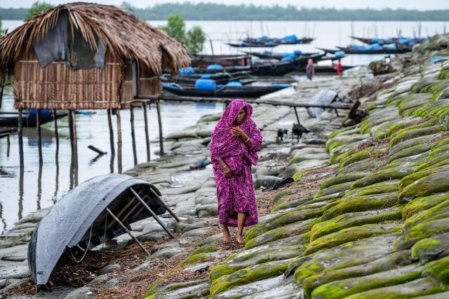 In this photograph taken on July 13, 2025, a climate-displaced woman walks over geo-textile bags along the Shibsa river at New Jhulonto Para, a village vulnerable to rising sea levels in Khulna district. On Bangladesh's coast, where mighty Himalayan rivers meet the sea, water defines every rhythm of life and every struggle. For the millions living in the ecologically sensitive deltas of mudflats and mangrove forests, finding clean drinking water has become an escalating challenge. Rising seas driven by climate change are swallowing low-lying areas, while stronger storms push saltwater further inland, turning wells and lakes brackish, according to government scientists. (Photo by Muhammad Amdad HOSSAIN / AFP) / To go with 'BANGLADESH-ENVIRONMENT-CLIMATE-WATER, REPORTAGE' by Muhammad Amdad HOSSAIN