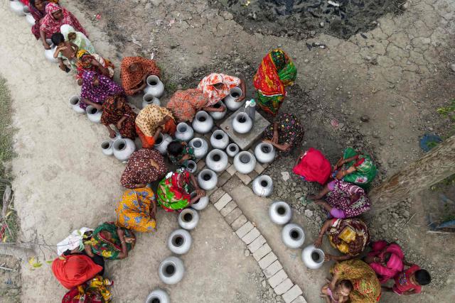 In this photograph taken on April 25, 2025, women queue to fetch pots of drinking water from a tap with intermittent water supply, installed by an NGO (non-governmental organization) at Parshemari village in Khulna district. On Bangladesh's coast, where mighty Himalayan rivers meet the sea, water defines every rhythm of life and every struggle. For the millions living in the ecologically sensitive deltas of mudflats and mangrove forests, finding clean drinking water has become an escalating challenge. Rising seas driven by climate change are swallowing low-lying areas, while stronger storms push saltwater further inland, turning wells and lakes brackish, according to government scientists. (Photo by Muhammad Amdad HOSSAIN / AFP) / To go with 'BANGLADESH-ENVIRONMENT-CLIMATE-WATER, REPORTAGE' by Muhammad Amdad HOSSAIN