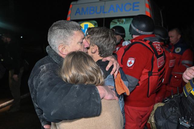 A man embraces his children in front of an emergency vehicle at the site of a Russian drone strike in Kharkiv late on November 23, 2025, amid the Russian invasion of Ukraine. A Russian drone strike on the major Ukrainian city of Kharkiv killed four people and wounded 17 on November 23, its mayor said. The attack came as US, Ukrainian and European officials were in Geneva to discuss a proposal to end the nearly four-year war in Ukraine, which began when Russia launched a full-scale invasion. (Photo by SERGEY BOBOK / AFP)