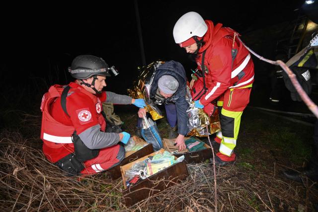 Paramedics help a local resident close to his destroyed house at the site of a Russian drone strike in Kharkiv late on November 23, 2025, amid the Russian invasion of Ukraine. A Russian drone strike on the major Ukrainian city of Kharkiv killed four people and wounded 17 on November 23, its mayor said. The attack came as US, Ukrainian and European officials were in Geneva to discuss a proposal to end the nearly four-year war in Ukraine, which began when Russia launched a full-scale invasion. (Photo by SERGEY BOBOK / AFP)
