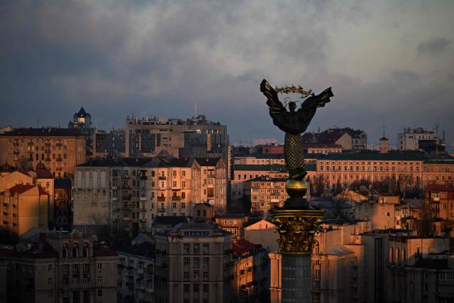 A photograph taken on November 24, 2025 shows The Independence Monument towers over Independence Square as buildings in the background are illuminated by a beam of sunlight during sunrise in Kyiv, amid the Russian invasion of Ukraine. (Photo by Sergei GAPON / AFP)