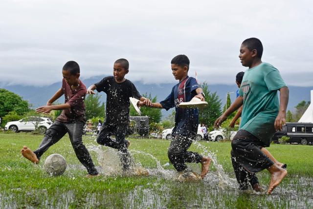 Youths play football in a flooded field following rain in Jantho, Aceh province on November 24, 2025. (Photo by CHAIDEER MAHYUDDIN / AFP)