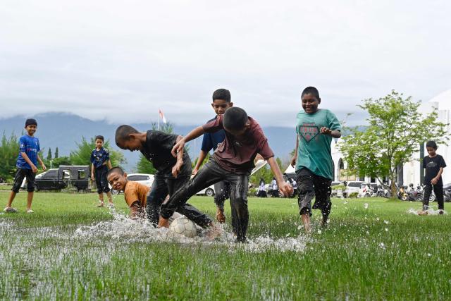Youths play football in a flooded field following rain in Jantho, Aceh province on November 24, 2025. (Photo by CHAIDEER MAHYUDDIN / AFP)