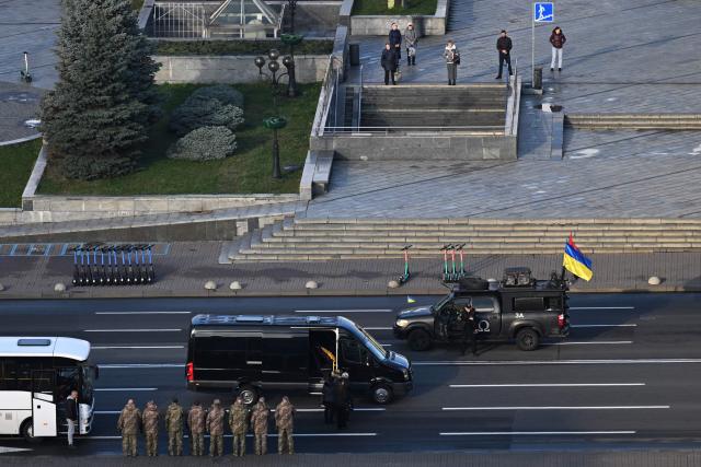 Pedestrians (top) observe a minute of silence as the body of a slain Ukrainian soldier is carried in a van on Independence Square in Kyiv on November 24, 2025, amid the Russian invasion of Ukraine. (Photo by Sergei GAPON / AFP)