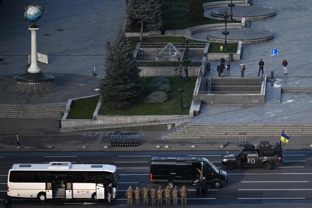 Pedestrians (top) observe a minute of silence as the body of a slain Ukrainian soldier is carried in a van on Independence Square in Kyiv on November 24, 2025, amid the Russian invasion of Ukraine. (Photo by Sergei GAPON / AFP)