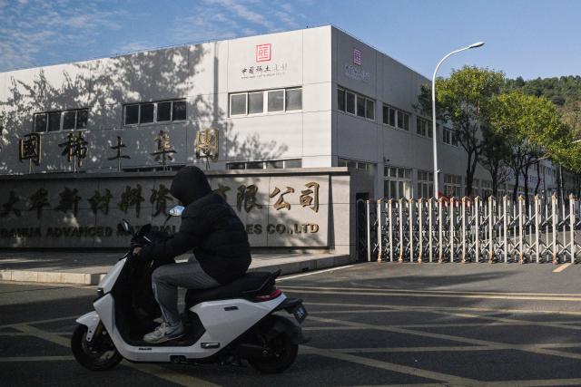 A motorist rides past as the logo of the China Rare Earth Group is seen on a building at a processing plant in Dingnan County, Ganzhou, in eastern China's Jiangxi province on November 20, 2025. (Photo by Hector RETAMAL / AFP)
