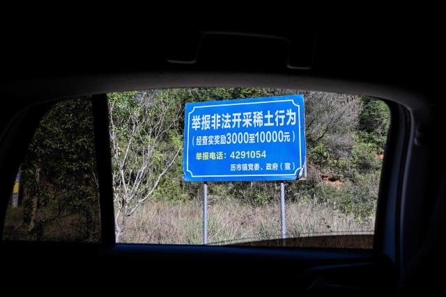 Signage announcing a reward for those who report illegal rare earth mining activities is seen in Dingnan County, Ganzhou, in eastern China's Jiangxi province on November 20, 2025. (Photo by Hector RETAMAL / AFP)