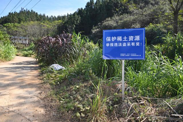 Signage announcing a reward for those who report illegal rare earth mining activities is seen in Dingnan County, Ganzhou, in eastern China's Jiangxi province on November 20, 2025. (Photo by Hector RETAMAL / AFP)