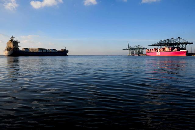A photograph taken on November 21, 2025 shows a container ship sailing past the Japanes "One Mackinac" container ship moored in the Port of Antwerp-Bruges, in Antwerp. (Photo by Nicolas TUCAT / AFP)
