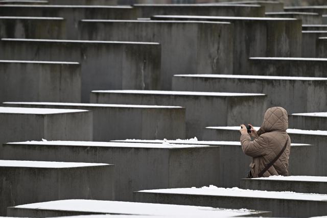 A woman takes pictures of Berlin's Holocaust Memorial after first snow of the season fell on the German capital on November 24, 2025. The Memorial to the Murdered Jews of Europe, designed by US architect Peter Eisenman, is made up of 2711 concrete steles forming a curved landscape in the heart of the capital. (Photo by John MACDOUGALL / AFP)