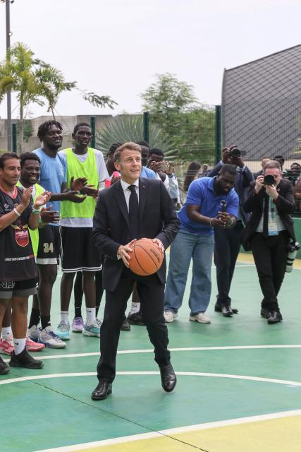 France’s President Emmanuel Macron (C) prepares to shoot for the basket while visiting a  basketball court with athletes in Libreville on November 24, 2025. (Photo by Ludovic MARIN / AFP) / ALTERNATE CROP