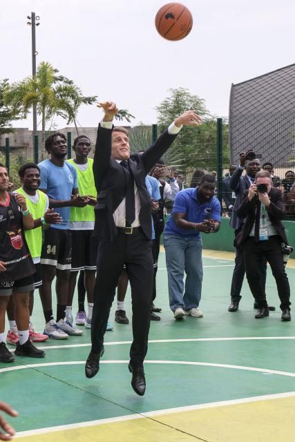 France’s President Emmanuel Macron (C) prepares to shoot for the basket while visiting a  basketball court with athletes in Libreville on November 24, 2025. (Photo by Ludovic MARIN / AFP) / ALTERNATE CROP