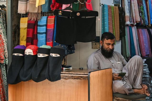 A shopkeeper selling niqab or face veils waits for customers at a market in Karachi on November 24, 2025. (Photo by Asif HASSAN / AFP)