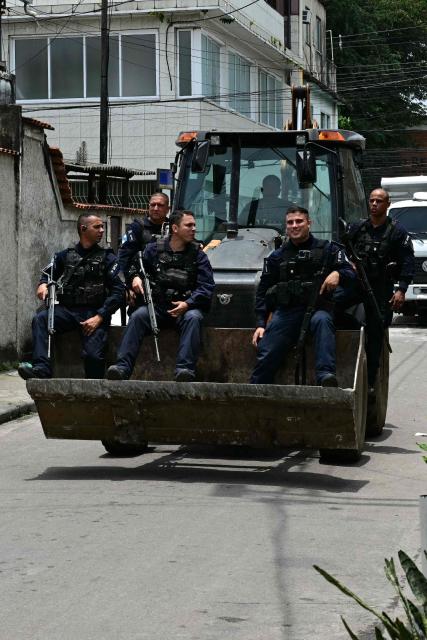 Military policemn are transported on a backhoe during an operation to dismantle barricades set up by criminals at the Cidade de Deus favela in Rio de Janeiro, Brazil, on November 24, 2025. (Photo by Pablo PORCIUNCULA / AFP)