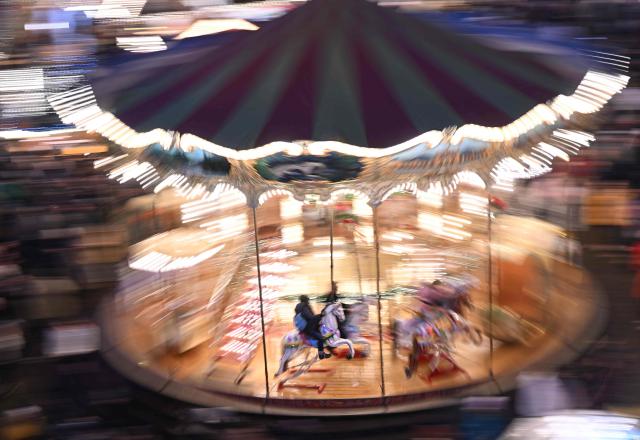 People sit on a merry-go-round at the Christmas market at the central Roemer square in Frankfurt am Main, on November 24, 2025. (Photo by Kirill KUDRYAVTSEV / AFP)
