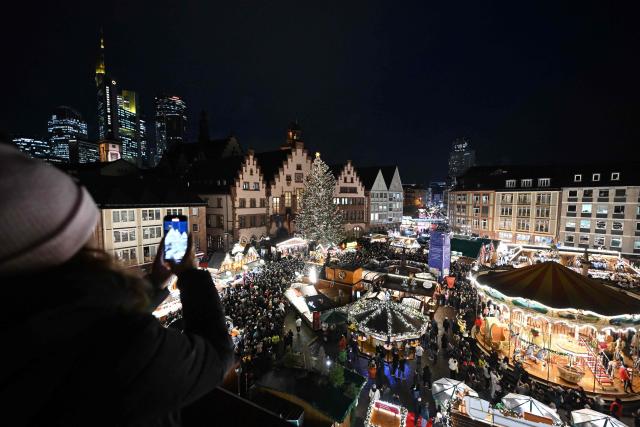A woman takes a picture of the Christmas market at the central Roemer square in Frankfurt am Main, on November 24, 2025. (Photo by Kirill KUDRYAVTSEV / AFP)
