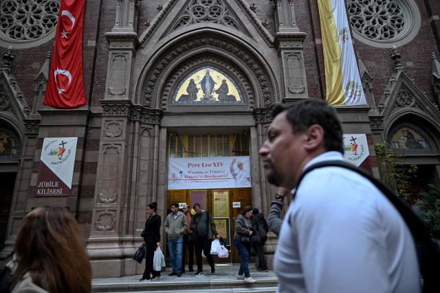 People walk outside the Saint Anthony of Padua Church# as a welcome banner bearing a portrait of Pope Leo XIV is displayed on its gate, ahead of his visit to Turkey, in Istanbul on November 24, 2025. (Photo by Ozan KOSE / AFP)